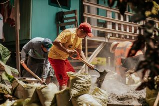 Men working energetically on construction, shoveling sand into bags outdoors.