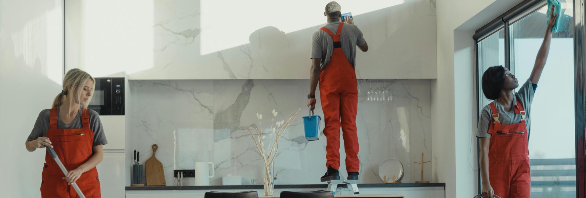 Group of cleaners in red uniforms mopping and wiping glass in a modern dining room.